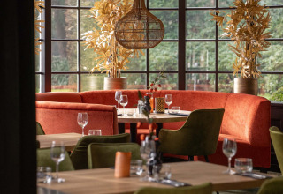Chic restaurant interior at Landgoed de Scheleberg holiday park, featuring orange sofas, green chairs, and large windows.