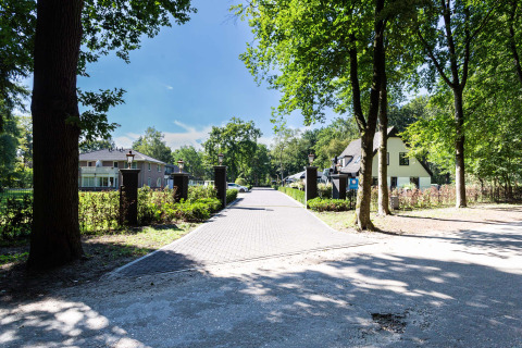 Zufahrt zum Ferienpark Résidence Lage Vuursche in Utrecht, Niederlande, mit Bäumen und modernen Häusern.