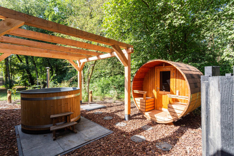 Outdoor spa area with a wooden hot tub and barrel sauna surrounded by nature at a Utrecht holiday park.