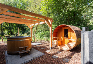 Outdoor spa area with a wooden hot tub and barrel sauna surrounded by nature at a Utrecht holiday park.