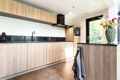 Cocina moderna con gabinetes de madera, encimeras negras y un jarrón de flores en Résidence Lage Vuursche.