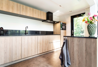 Moderne keuken met houten kasten, zwart werkblad en bloemenvaas bij Résidence Lage Vuursche, Utrecht.