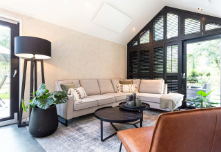Modern living room at Résidence Lage Vuursche, Utrecht, with a sectional sofa, large windows and plants.