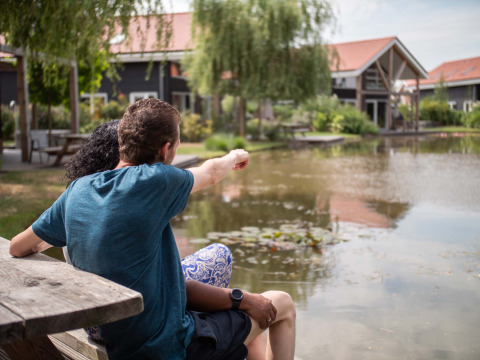 Et par sidder ved en dam og nyder udsigten på Résidence Lichtenvoorde feriepark i Gelderland, Holland.