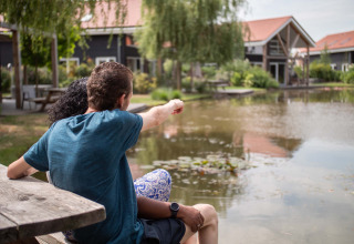 Et par sidder ved en dam og nyder udsigten på Résidence Lichtenvoorde feriepark i Gelderland, Holland.