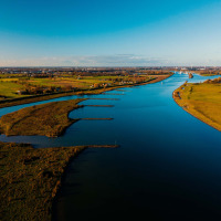 Vista aérea de un río serpenteante y campos verdes cerca de Lage Vuursche, Utrecht, Países Bajos, con cielo azul.