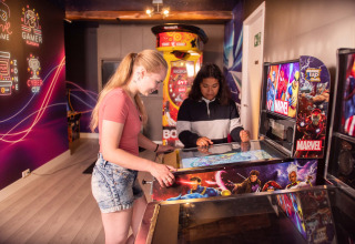 Twee meisjes spelen op een Marvel-flipperkast in de levendige speelhal van Résidence Valkenburg, Nederland.