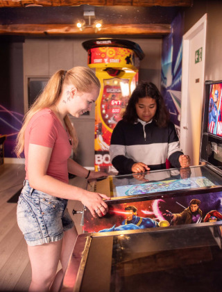 Zwei Mädchen spielen an einem Marvel-Flipperautomaten im bunten Spieleraum von Résidence Valkenburg.