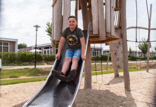 Junge rutscht auf einer Rutsche im Spielplatz vor einem Holzhaus in Résidence Valkenburg, Limburg, Niederlande.