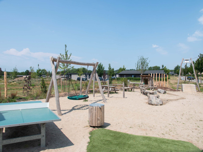 Speeltuin met schommel, tafeltennistafel en zand in een vakantiepark in Limburg, Nederland.