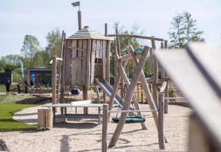 Holzspielplatz mit Rutsche und Schaukel im Ferienpark Résidence Valkenburg in Limburg, Niederlande, tagsüber.