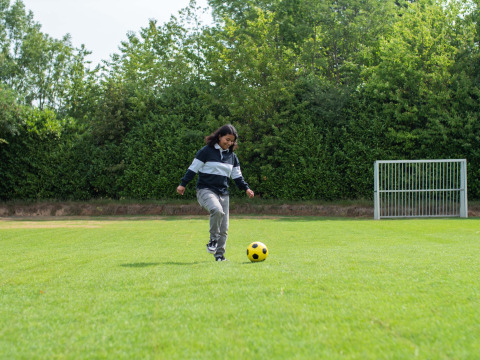 A person kicks a yellow soccer ball on a green field at Résidence Valkenburg in Limburg, Netherlands.