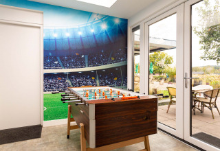 Spielzimmer mit Tischfußball, Wandbild eines vollen Fußballstadions und Zugang zur Gartenterrasse.