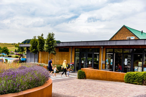 Gezin wandelt voorbij de receptie van Résidence Valkenburg, een vakantiepark in Limburg, Nederland, met groen.