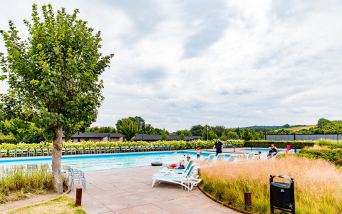 Buitenzwembad met ligzetels en mensen die relaxen in Résidence Valkenburg vakantiepark, Limburg, Nederland.