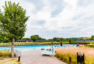 Outdoor swimming pool with lounge chairs and people relaxing at Résidence Valkenburg holiday park in Limburg, Netherlands.