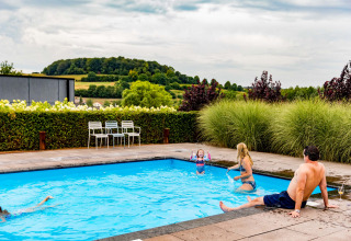 Famille profitant d'une piscine extérieure à la Résidence Valkenburg, entourée du paysage vallonné du Limbourg.