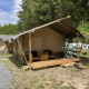 Safari telt med træveranda og havemøbler, placeret i en skovlysning med andre telte i baggrunden.