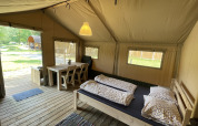 Vista interior de una tienda safari en Camping du Rivage en Luxemburgo, con cama, mesa y suelo de madera.