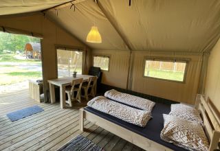 Vista interior de una tienda safari en Camping du Rivage en Luxemburgo, con cama, mesa y suelo de madera.