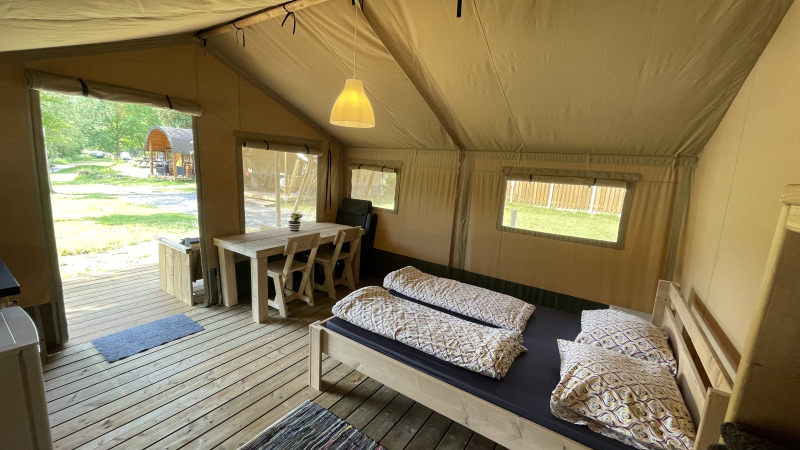 Vista interior de una tienda safari en Camping du Rivage en Luxemburgo, con cama, mesa y suelo de madera.
