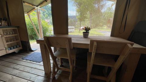 Interior view of a safari tent at Camping du Rivage in Luxembourg, with wooden table, chairs, and outside view.