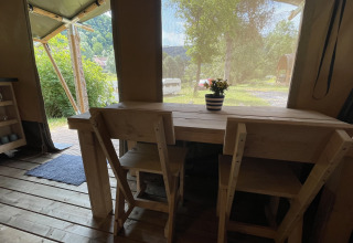 Vista interna di una tenda safari al Camping du Rivage in Lussemburgo, tavolo in legno, sedie e vista esterna.