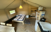 Intérieur d’une tente safari au Camping du Rivage au Luxembourg, avec lit, cuisine et coin repas.