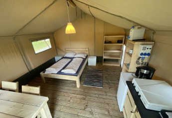 Interior de una tienda safari en Camping du Rivage en Luxemburgo con cama, cocina y mesa comedor.