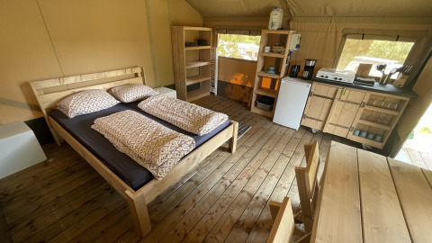 Interieur van een safaritent op Camping du Rivage in Luxemburg met bed, keuken en houten eethoek.