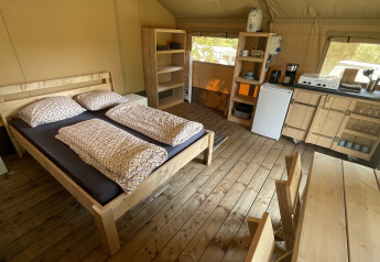 Interior of a safari tent at Camping du Rivage in Luxembourg with bed, kitchen, and wooden dining area.