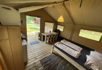 Vista interior de una tienda safari en Camping du Rivage en Luxemburgo, con cama y mesa de comedor.