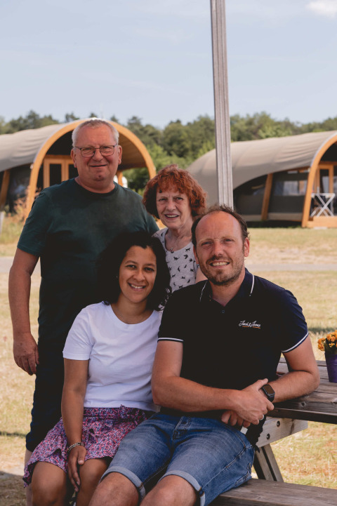 Cuatro personas sonrientes sentadas frente a tiendas glamping en Camping de Bovenberg en Overijssel, Países Bajos.