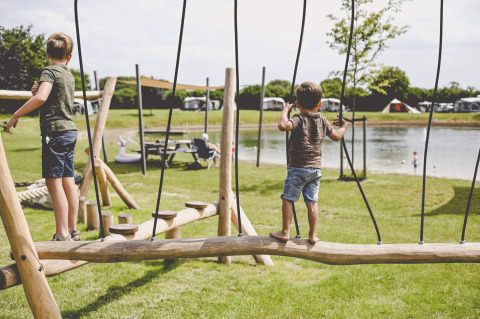 Due bambini giocano su un parco giochi di legno vicino a un lago al Camping de Bovenberg a Overijssel, Paesi Bassi.