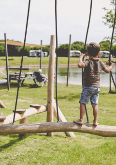Twee kinderen spelen op een houten speeltoestel bij een meer op Camping de Bovenberg in Overijssel, Nederland.