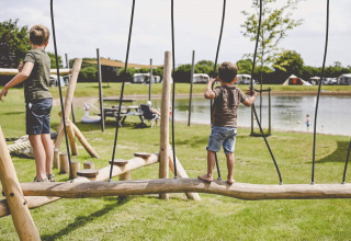 Zwei Kinder spielen auf einem Holzspielplatz am See im Ferienpark Camping de Bovenberg in Overijssel, Niederlande.