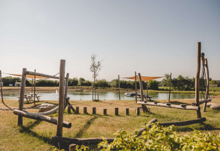 Spielplatz mit Holzelementen und Teich im Hintergrund auf Camping de Bovenberg, Overijssel, Niederlande.