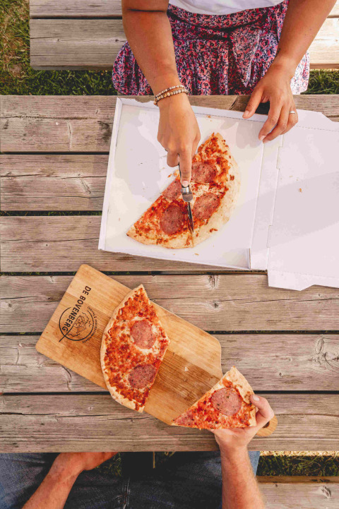 Twee mensen delen pizza op een houten tafel bij Camping de Bovenberg, Overijssel, Nederland.