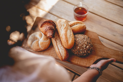 Eine Person hält ein Holzbrett mit verschiedenen Brotsorten und einer Tasse Tee im Ferienpark Bovenberg.