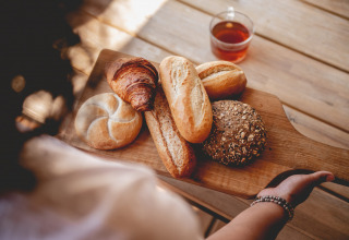 Eine Person hält ein Holzbrett mit verschiedenen Brotsorten und einer Tasse Tee im Ferienpark Bovenberg.