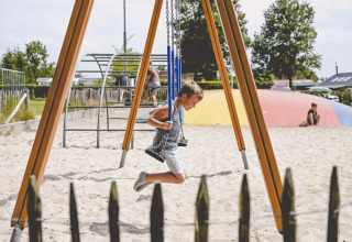 Junge schaukelt auf einem Sandspielplatz im Camping de Bovenberg, Overijssel, Niederlande, sonniger Tag.