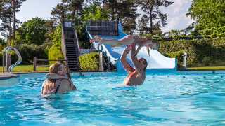 Familia disfruta nadando y jugando en Resort Veluwe, un parque vacacional en Gelderland, Países Bajos, con tobogán.