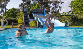Familia disfruta nadando y jugando en Resort Veluwe, un parque vacacional en Gelderland, Países Bajos, con tobogán.