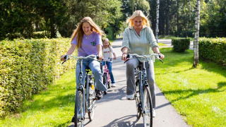 Familia paseando en bicicleta por un sendero soleado en Resort Veluwe, un parque vacacional en Gelderland, Holanda.