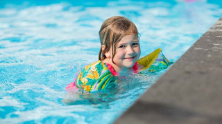 Niña sonriente con flotadores coloridos nada en la piscina del Recreatiepark Beekbergen, Gelderland.