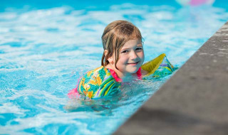 Niña sonriente con flotadores coloridos nada en la piscina del Recreatiepark Beekbergen, Gelderland.