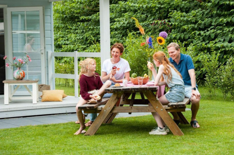 Family enjoys an outdoor meal at a wooden table near Verandah Chalet at Camping Sevink Molen, Netherlands.