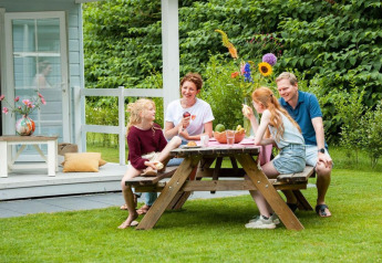 Familie nyder måltid udendørs ved et bord foran Verandah Chalet på Camping Sevink Molen, Holland.
