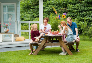 Familie genießt eine Mahlzeit im Freien vor Verandah Chalet am Camping Sevink Molen, Niederlande.