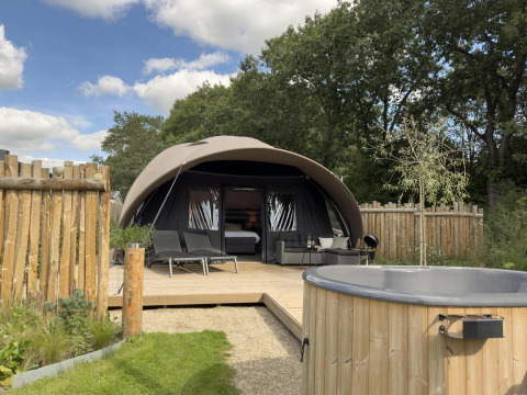 Alojamiento tipo tienda moderna con terraza, tumbonas y jacuzzi de madera, rodeado de naturaleza y vallado.